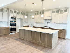 Kitchen with sink, hanging light fixtures, light hardwood / wood-style floors, a kitchen island with sink, and appliances with stainless steel finishes