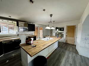 Kitchen with dark wood-type flooring, hanging light fixtures, butcher block countertops, backsplash, and a kitchen island