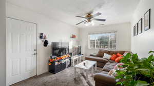 Living room featuring carpet flooring, ceiling fan, a textured ceiling, and ornamental molding