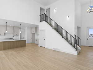 Unfurnished living room with a towering ceiling, an inviting chandelier, light hardwood / wood-style flooring, and sink