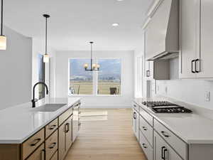 Kitchen with pendant lighting, sink, premium range hood, and an island with sink