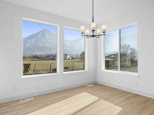 Unfurnished dining area with hardwood / wood-style flooring, a mountain view, a healthy amount of sunlight, and an inviting chandelier