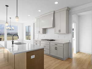 Kitchen with light wood-type flooring, custom exhaust hood, a kitchen island with sink, sink, and a chandelier