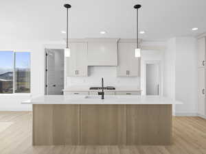 Kitchen with pendant lighting, white cabinetry, and an island with sink