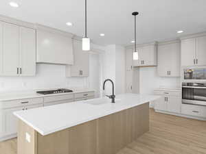 Kitchen featuring stainless steel appliances, a kitchen island with sink, sink, decorative light fixtures, and light hardwood / wood-style flooring