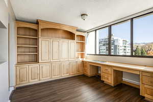 Unfurnished office featuring dark hardwood / wood-style floors, built in desk, and a textured ceiling