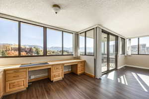 Unfurnished office featuring a mountain view, a textured ceiling, built in desk, and dark hardwood / wood-style floors