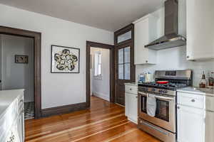 Kitchen featuring backsplash, stainless steel range with gas cooktop, wall chimney range hood, light hardwood / wood-style flooring, and white cabinetry