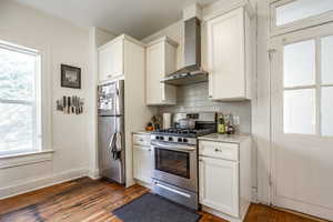 Kitchen with dark hardwood / wood-style flooring, stainless steel appliances, a wealth of natural light, and wall chimney range hood