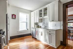 Kitchen featuring white cabinets, sink, light hardwood / wood-style flooring, decorative backsplash, and stainless steel appliances