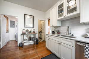 Kitchen with backsplash, stainless steel dishwasher, sink, light hardwood / wood-style flooring, and white cabinets