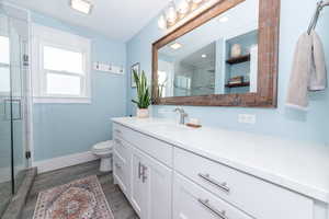 Bathroom featuring a shower with door, vanity, wood-type flooring, and toilet