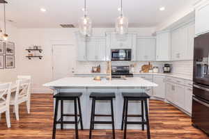 Kitchen with hardwood / wood-style flooring, a center island with sink, hanging light fixtures, and appliances with stainless steel finishes