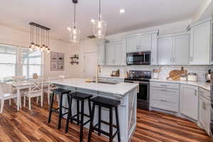 Kitchen featuring stainless steel appliances, light stone counters, dark hardwood / wood-style floors, and an island with sink