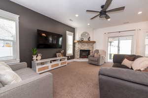 Living room featuring carpet flooring, a stone fireplace, and ceiling fan