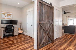 Office space with a barn door, ceiling fan, and dark hardwood / wood-style floors