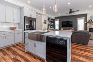 Kitchen with a stone fireplace, hardwood / wood-style flooring, decorative backsplash, black dishwasher, and light stone counters