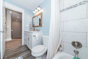 Full bathroom with hardwood / wood-style flooring, vanity, toilet, and shower / bath combo with shower curtain