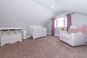 Carpeted bedroom featuring lofted ceiling and a crib