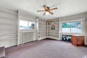 Unfurnished bedroom featuring carpet, ceiling fan, and radiator heating unit