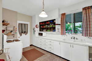 Kitchen with white cabinets, sink, hanging light fixtures, light tile patterned flooring, and washer / clothes dryer