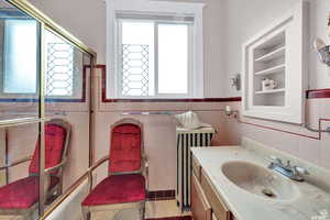 Bathroom with plenty of natural light, vanity, tile walls, and radiator