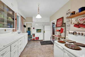 Kitchen with backsplash, tile countertops, decorative light fixtures, white fridge, and white cabinetry