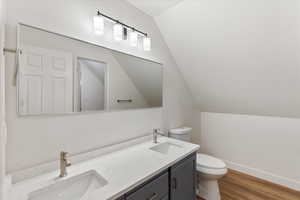 Bathroom with toilet, vanity, hardwood / wood-style flooring, and vaulted ceiling