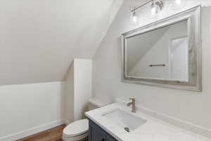 Bathroom featuring hardwood / wood-style flooring, vanity, toilet, and vaulted ceiling