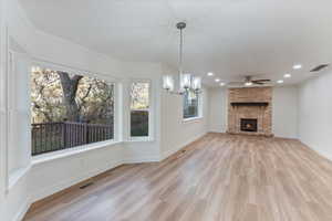 Unfurnished living room with ceiling fan with notable chandelier, light hardwood / wood-style floors, crown molding, and a fireplace