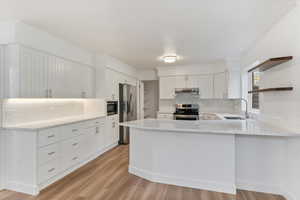 Kitchen with white cabinets, stainless steel appliances, kitchen peninsula, and light hardwood / wood-style floors