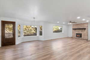 Unfurnished living room with a brick fireplace, light hardwood / wood-style flooring, a textured ceiling, ceiling fan with notable chandelier, and ornamental molding