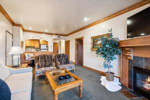 Carpeted living room with a tiled fireplace and crown molding