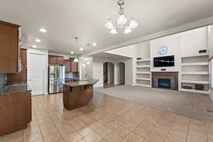 Kitchen featuring built in shelves, light carpet, pendant lighting, a kitchen island with sink, and appliances with stainless steel finishes