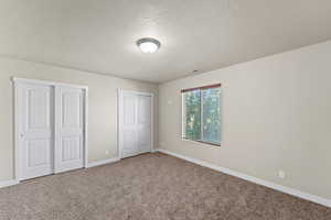 Unfurnished bedroom featuring a textured ceiling, carpet floors, and two closets