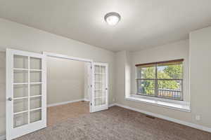 Carpeted empty room with french doors and a textured ceiling