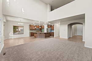 Unfurnished living room featuring light carpet, a high ceiling, a chandelier, and sink