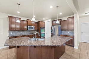 Kitchen featuring appliances with stainless steel finishes, an island with sink, hanging light fixtures, and sink