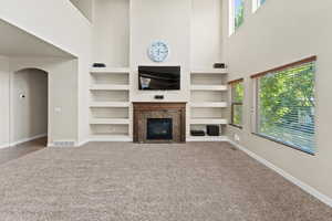 Unfurnished living room with carpet flooring, plenty of natural light, built in features, and a towering ceiling