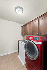 Laundry room featuring washer and clothes dryer, cabinets, light tile patterned floors, and a textured ceiling