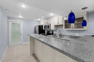 Kitchen featuring kitchen peninsula, a textured ceiling, stainless steel appliances, sink, and hanging light fixtures