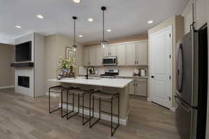 Kitchen featuring sink, an island with sink, decorative light fixtures, appliances with stainless steel finishes, and light wood-type flooring.Under Construction. Pictures of a model for example only. Colors and other features may vary from picture.