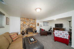 Carpeted living room featuring a stone fireplace and a textured ceiling