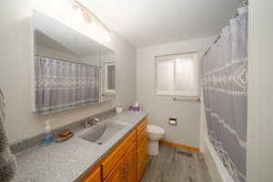 Full bathroom with shower / bath combo with shower curtain, hardwood / wood-style floors, vanity, and toilet