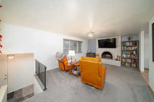 Living room featuring carpet, a textured ceiling, and a brick fireplace