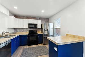 Kitchen with black appliances, sink, blue cabinetry, and light hardwood / wood-style flooring