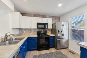 Kitchen with black appliances, blue cabinets, sink, light hardwood / wood-style floors, and white cabinetry