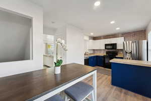 Kitchen featuring blue cabinetry, light hardwood / wood-style flooring, backsplash, white cabinets, and black appliances