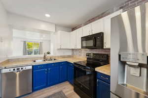 Kitchen with sink, blue cabinets, light hardwood / wood-style floors, white cabinets, and black appliances