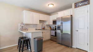 Kitchen featuring sink, appliances with stainless steel finishes, light hardwood / wood-style floors, white cabinetry, and a breakfast bar area